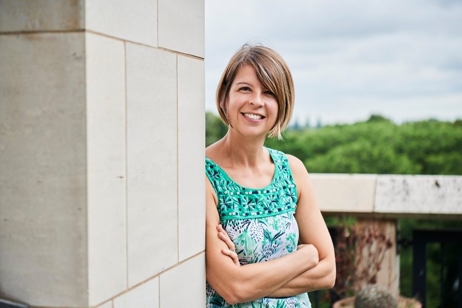 Woman leant against an outside wall smiling at the camera