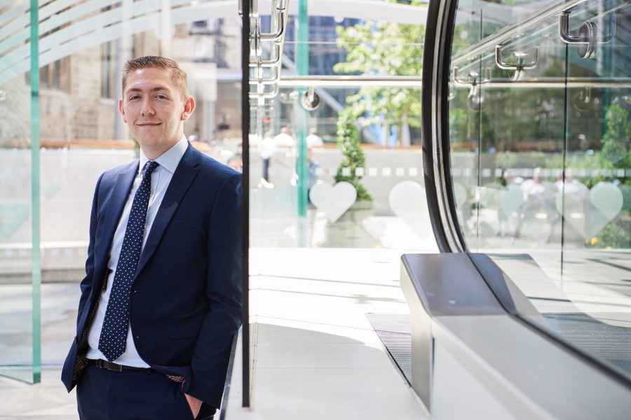 Man in a suit smiling to camera stood in the atrium at St Helen's, London