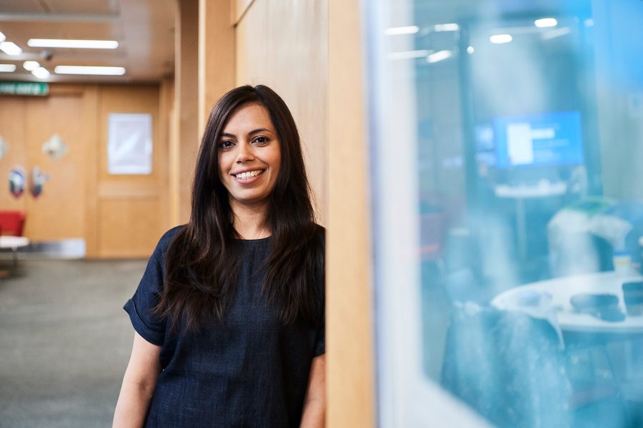 Woman smiling to camera leaning against wall in an office environment