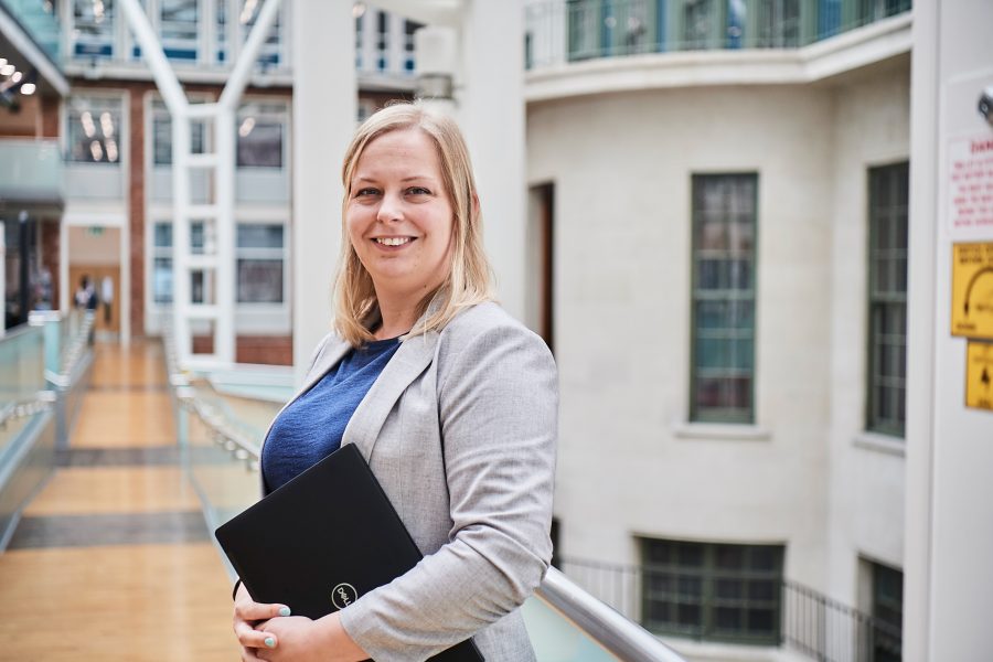 Woman stood in office with laptop smiling at camera